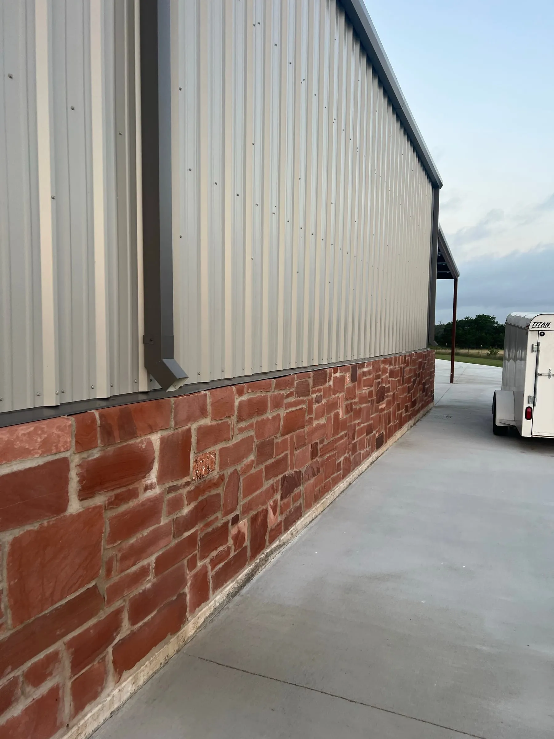 Metal siding with dark trim and a red stone base beside the concrete walkway.