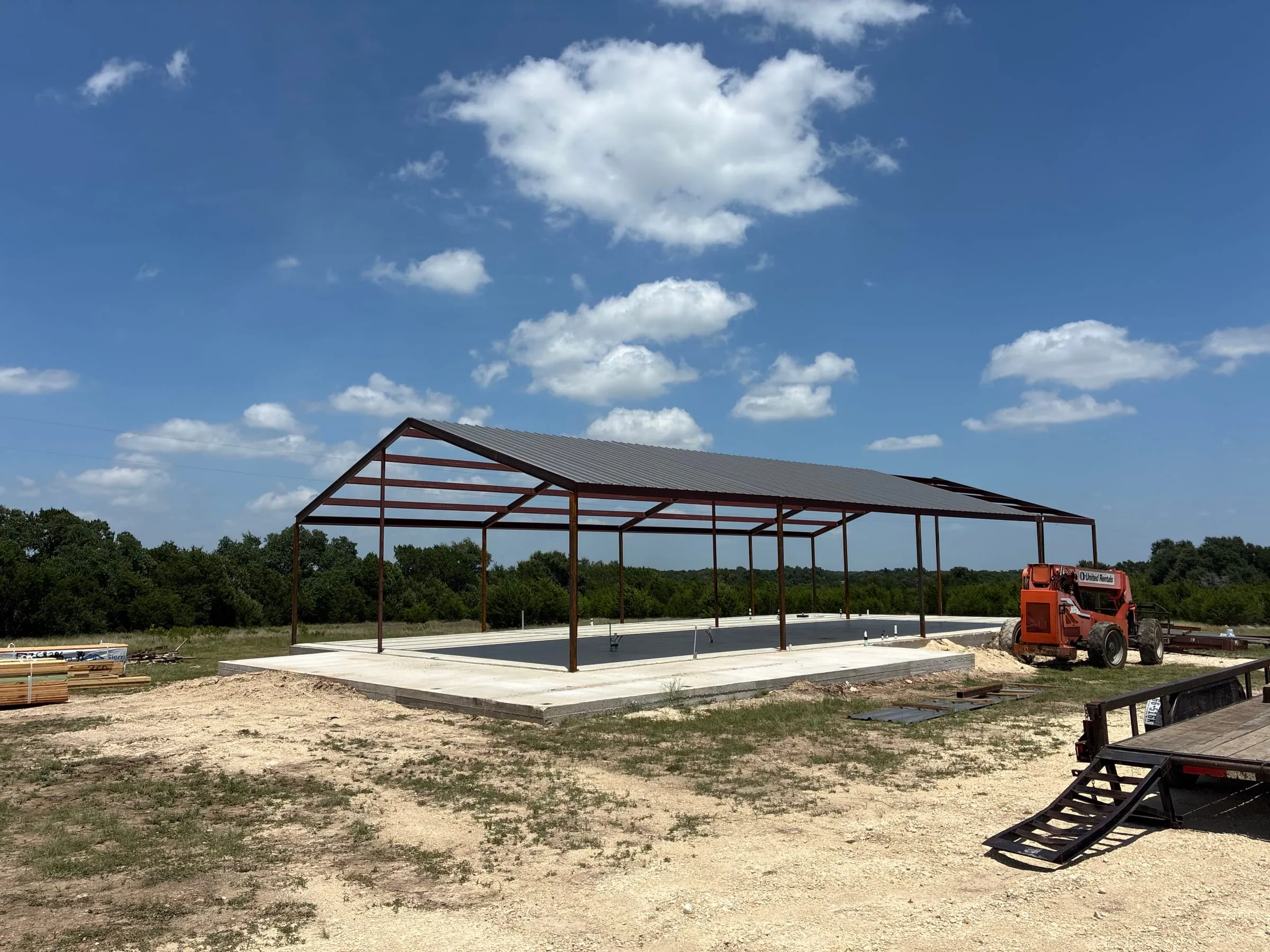 Open steel shop extension standing over a rectangular concrete slab.
