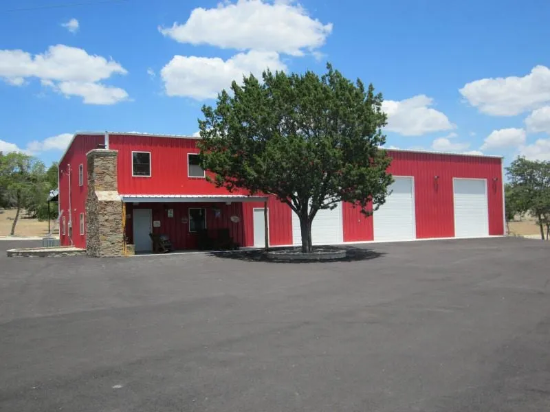 Red custom steel home with metal siding, stone entry, and covered parking.